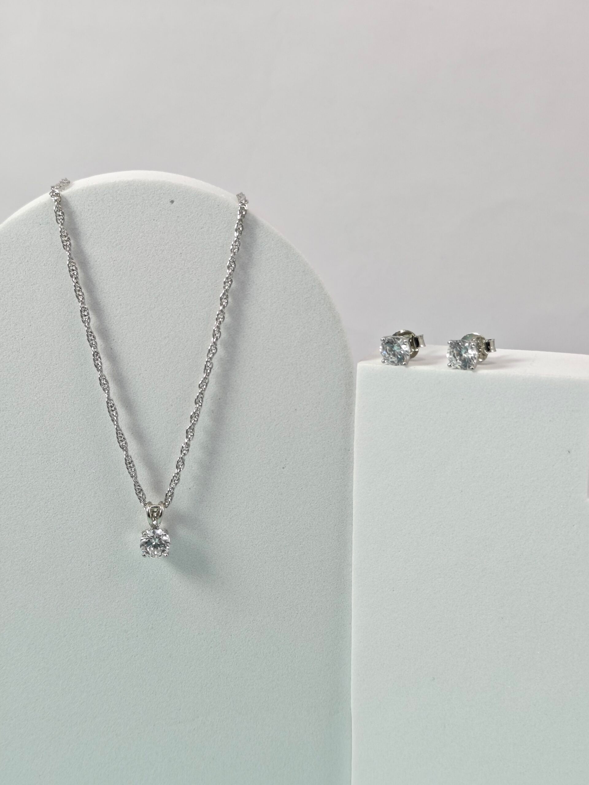 Silver necklace and earrings on a white stand against a light gray background